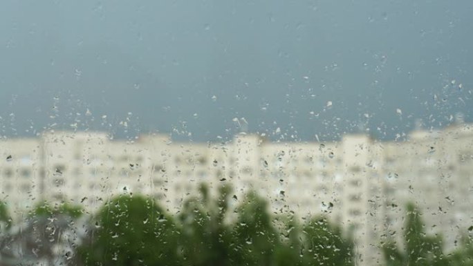 窗户玻璃上的水滴。城市的夏雨，蓝天，房屋和绿树的模糊轮廓。4k视频