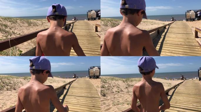 儿童男孩在木制小路追踪镜头上走向海滩