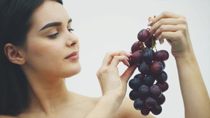 一个漂亮苗条的女孩吃健康的水果。一个漂亮的年轻女人的肖像拿着一束成熟的葡萄和一个真理。