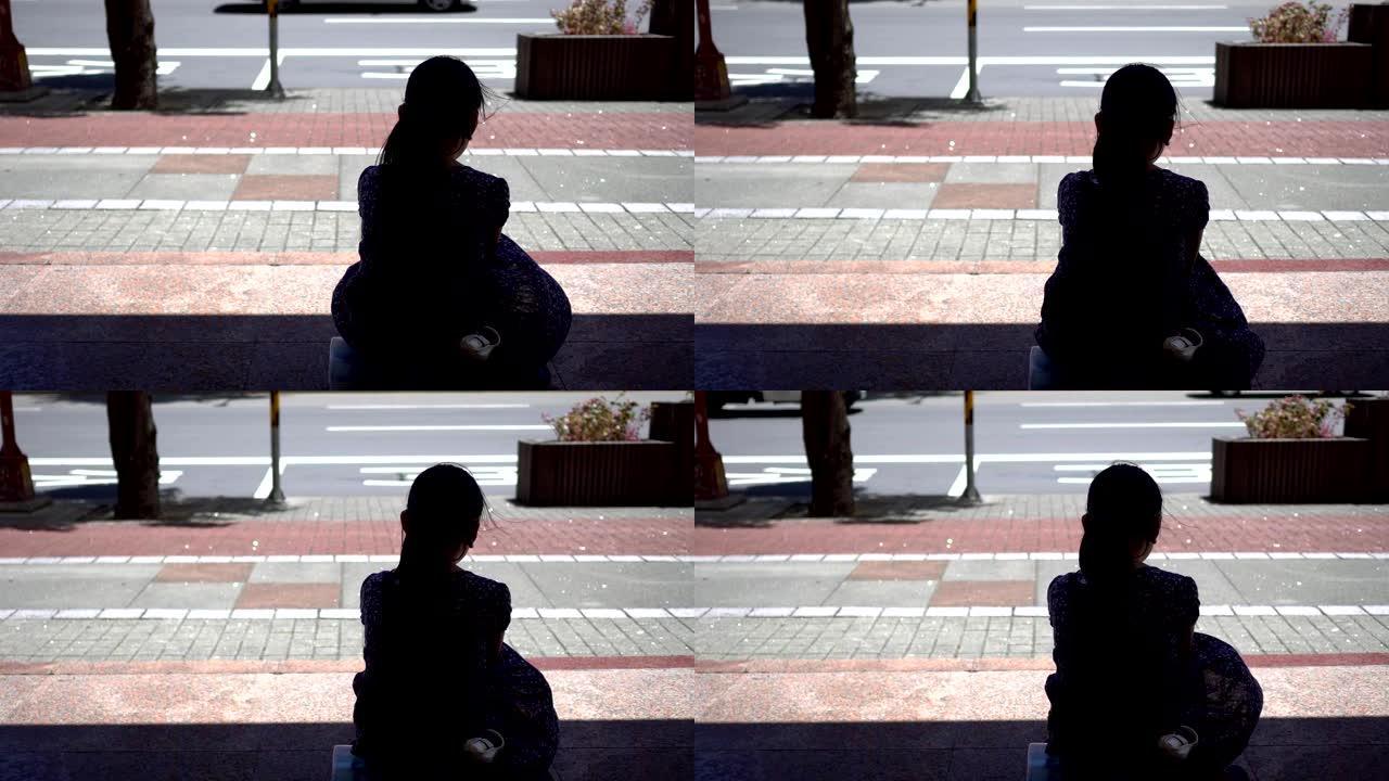 坐在公共汽车站的小女孩的剪影。