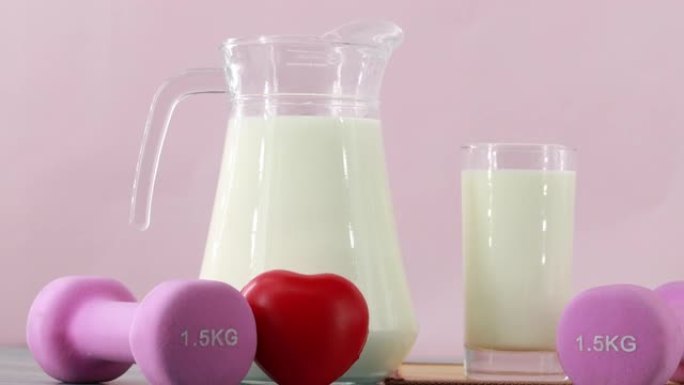 在粉红色背景上关闭装有玻璃牛奶和哑铃的罐子。早餐健康，锻炼健康。多莉拍摄幻灯片