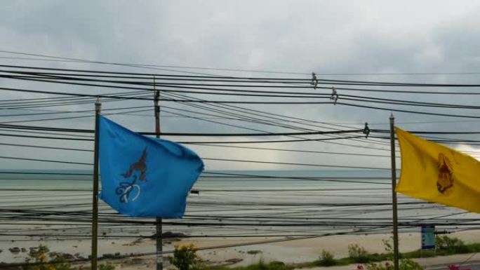 阴天在海边挥舞旗帜。阴天沿海岸悬挂泰国及王室彩旗。背景上杂乱的电线。国家和泰国民族的象征。