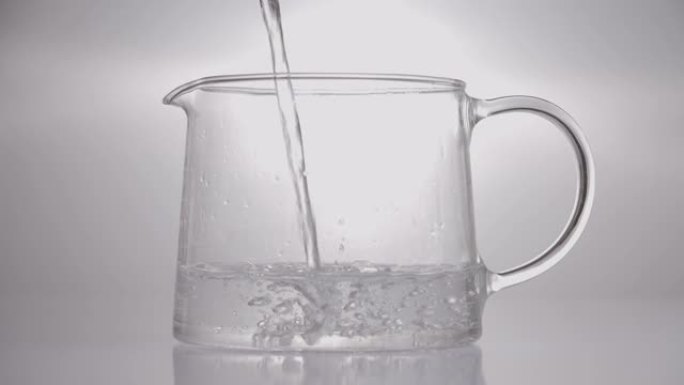 将热水倒入玻璃透明罐子中。孤立，在灰色背景上
