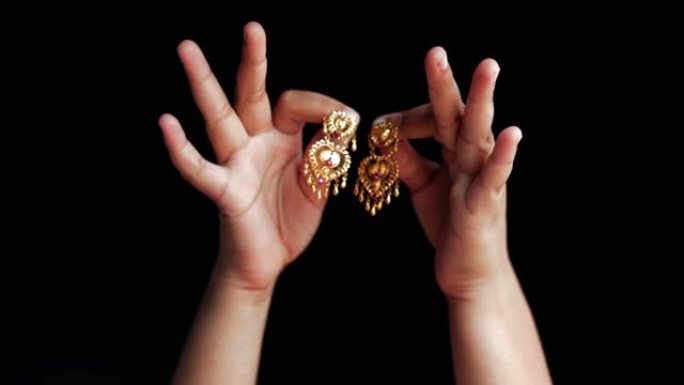 一对十几岁的女性双手，露出金色的印度风格耳环，孤立在黑色背景上。