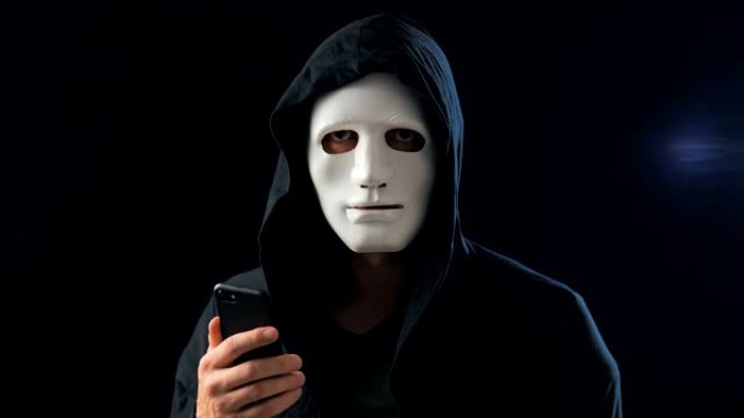 一名蒙面匿名诈骗犯使用智能手机进行勒索，要求赎金。蒙面罪犯利用手机短信威胁受害者。