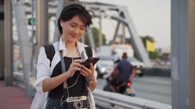 慢动作: 穿着白衬衫的微笑女人使用智能手机并在桥上行走