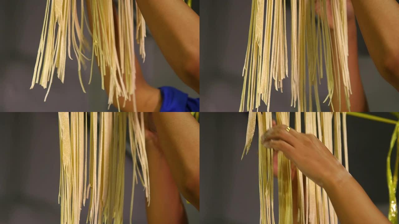 一位女厨师以慢动作将新鲜的意大利面条挂在黄色的绳子上。