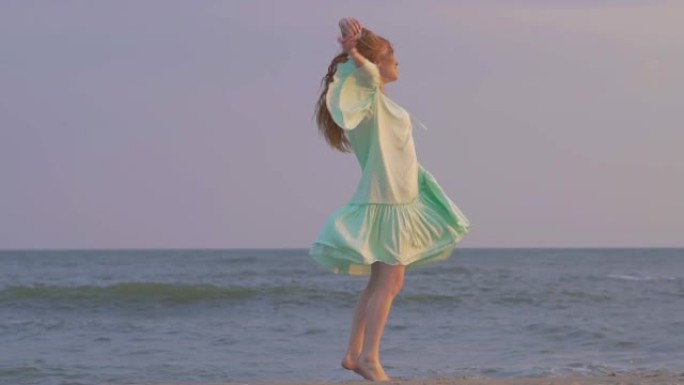无忧无虑的女人在海边的日落上跳舞。女孩旋转