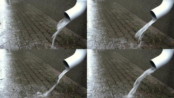 水从建筑物前部的白色排水管倒入铺路板上。阴沉的秋日在城市下雨。特写。侧视图。4K。