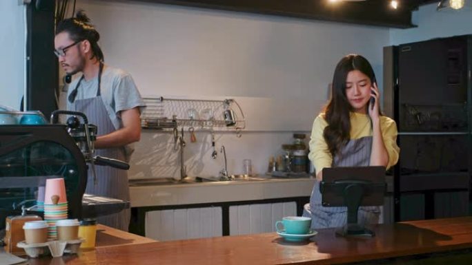 年轻的亚洲女性咖啡师，女服务员，小企业主在咖啡店咖啡馆柜台用数字平板电脑打电话点菜背景
