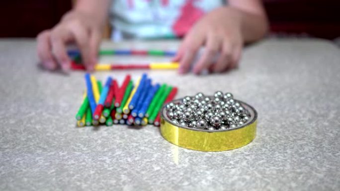小孩子在室内玩许多彩色磁铁玩具和铁球。