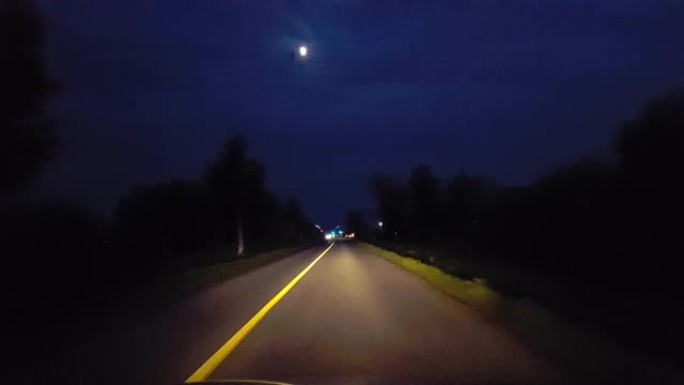 开车穿过乡村，接近地平线上的城市灯光。驾驶视点POV在夜间驶向进入城市极限。