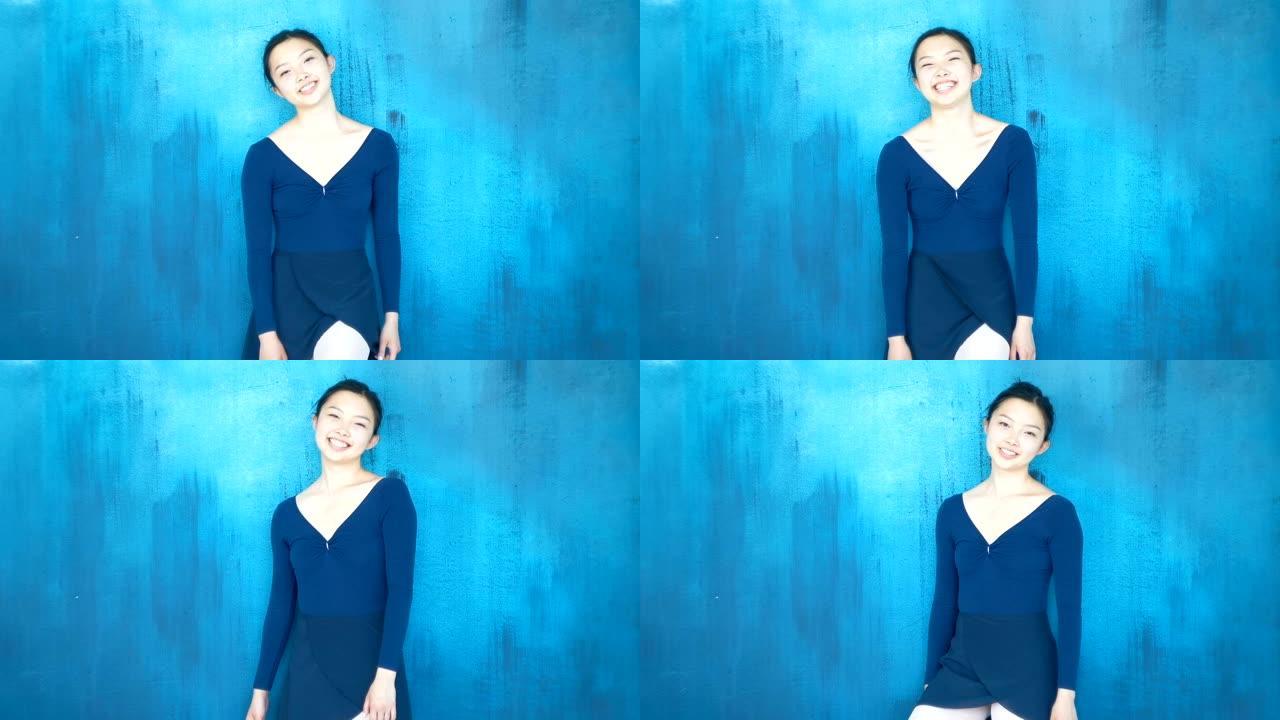 快乐的亚洲芭蕾舞女演员笑着看着蓝色背景上的相机