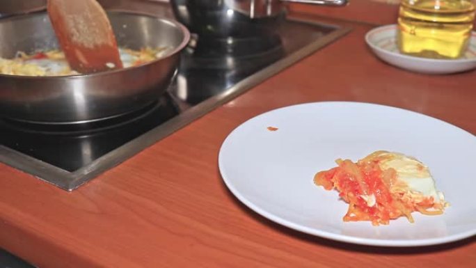 厨师将热气腾腾的煎蛋卷，碎鸡蛋，西红柿和洋葱放在盘子里