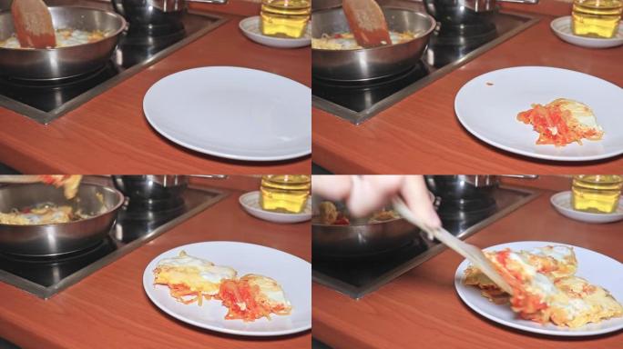 厨师将热气腾腾的煎蛋卷，碎鸡蛋，西红柿和洋葱放在盘子里