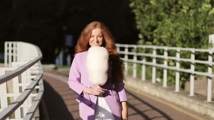 红发女孩手里拿着棉花糖穿过公园。
