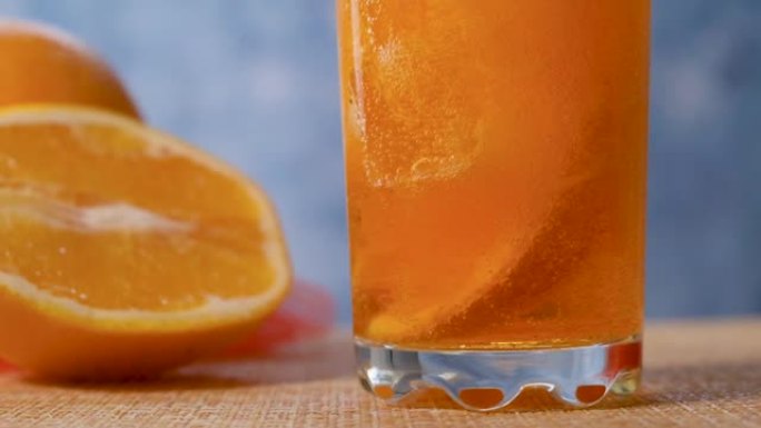 将黄色橙色柠檬水倒入装有橙色和冰的透明玻璃杯中。慢动作。