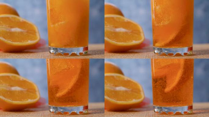 将黄色橙色柠檬水倒入装有橙色和冰的透明玻璃杯中。慢动作。