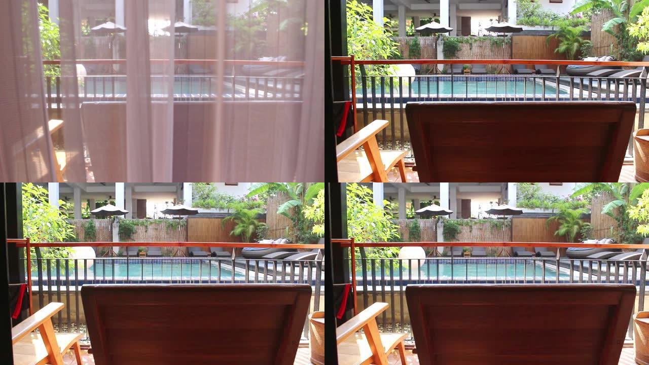 打开白色窗帘，从房间的阳台上可以看到游泳池的景色，并在度假胜地放轻松的椅子。