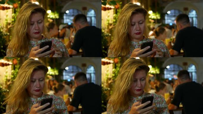 沉思的女孩使用智能手机，写一条消息，聊天。女人在电话里寻找信息而悲伤。独自坐在餐馆里。晚上时间，光线