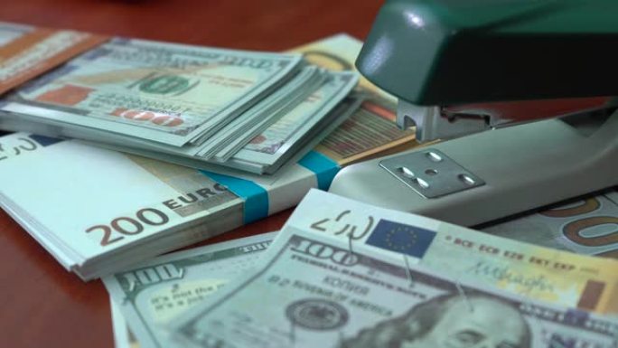 订书机用铁夹固定美元和欧元纸币。纸币背景上有回形针的订书机。假币