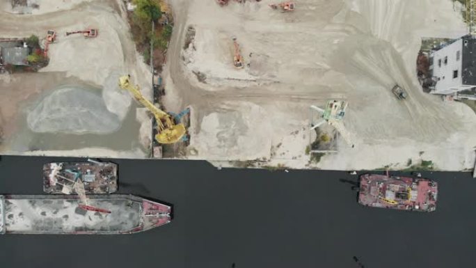 河岸上的港口起重机产生沙子。河岸上有铲斗的港口起重机。用卡车和挖掘机抽砂