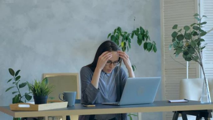 紧张的年轻女子在办公室使用破损的笔记本电脑感到恼火