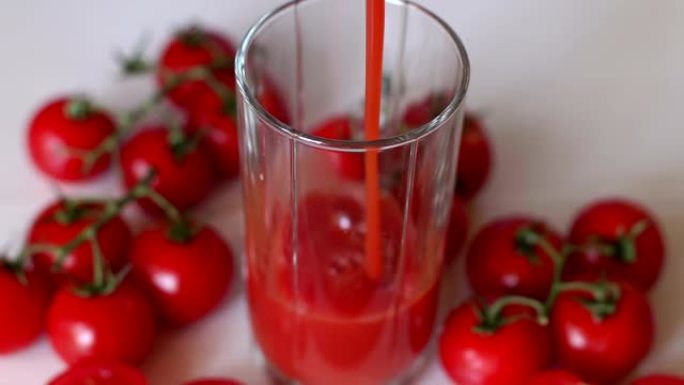 特写镜头将番茄汁倒入空玻璃杯中，放在新鲜的樱桃番茄旁边