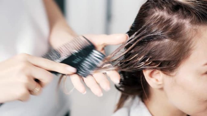 美发师手在年轻女性头发上涂抹发膜的特写