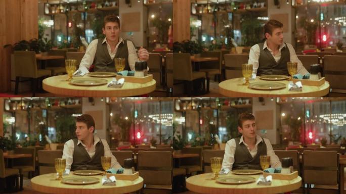 英俊的年轻人坐在餐馆里等着。现代餐厅，晚餐。侧面摄像机跨度。