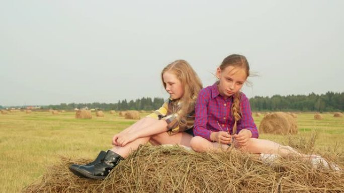 十几岁的女孩坐在山顶干草堆上。严肃的少女在收割田里思考干草堆。女朋友在农田里放松。