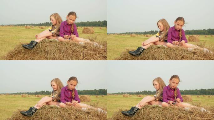 十几岁的女孩坐在山顶干草堆上。严肃的少女在收割田里思考干草堆。女朋友在农田里放松。