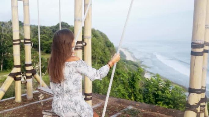 年轻女子在秋千上摇摆的背面视图，海洋美景，慢动作