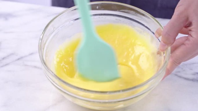 用绿色硅胶刮刀将蛋黄混合到雪纺蛋糕面糊中搅拌工具搅拌直至光滑，并在玻璃碗中充分混合，4k特写视图。