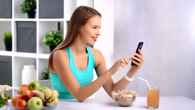 热情快乐的女孩在厨房吃早餐时用智能手机聊天