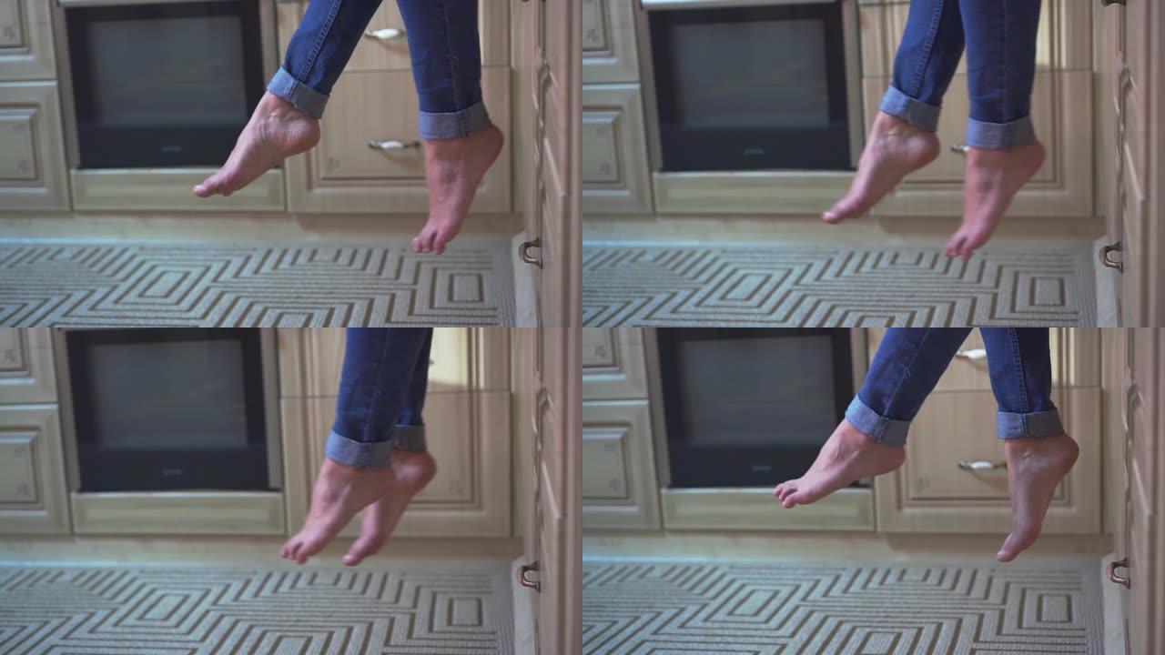 厨房里一个女孩腿的特写。这个女孩穿着蓝色牛仔裤，摇晃着双腿。