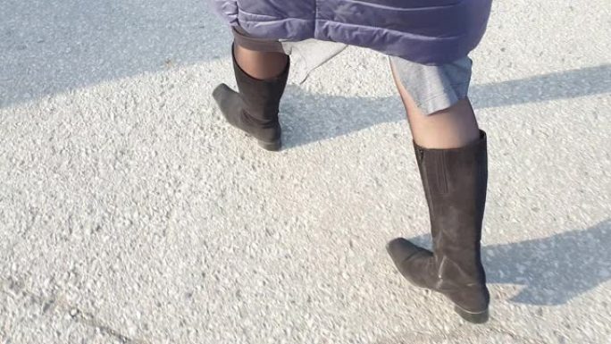 穿着麂皮靴子的女人的脚在沥青上