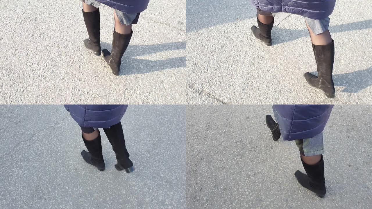 穿着麂皮靴子的女人的脚在沥青上