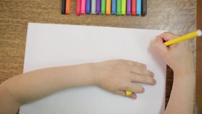 孩子用黄色的毡尖笔在白纸上画画。儿童用毡尖笔绘制特写。这个男孩画了一个黄色的太阳。