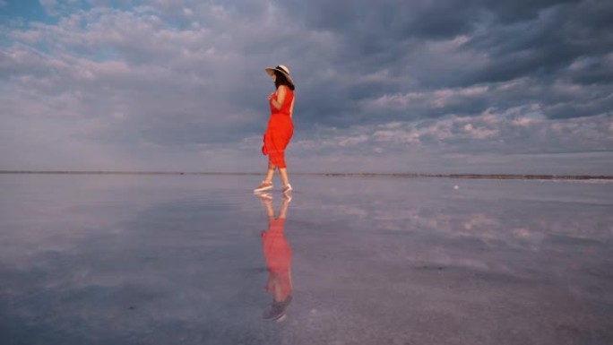 女孩在一个粉红色的盐湖上漫步，湖面上倒映着天空