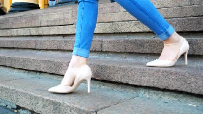 穿着牛仔裤的女性腿和时髦的高跟鞋下楼。迷人女孩踩在楼梯上的苗条脚。年轻女子在楼梯上下降。走在城市街道