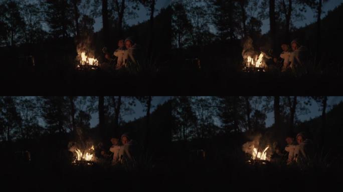 一对年轻夫妇晚上坐在森林里，在篝火前的普通格子下拥抱，有说有笑
