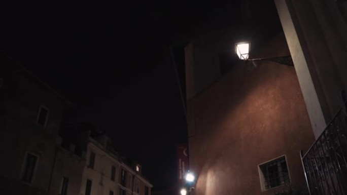 夜间在高楼的古罗马街道上闪烁路灯。市中心中世纪房子的历史立面。晚上空荡荡的街道，照亮狭窄的街道。建筑