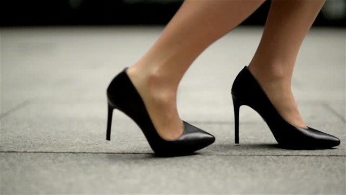 穿着高跟鞋的年轻女商人的脚进城。下班后，女商人穿着高跟鞋在办公室附近行走。慢动作