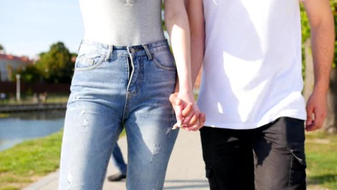 两个恋人携手的特写镜头。男人和女人牵手在公园散步的细节轮廓。夫妻信任、爱和幸福的概念。