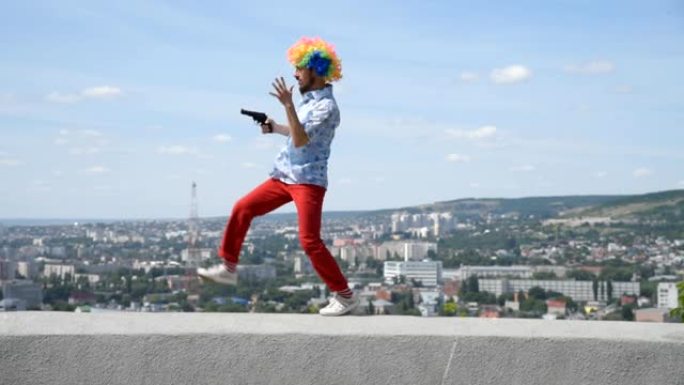 疯狂的哑剧手拿枪在栏杆上跳舞。在城市的背景下，一个带着手枪的小丑的有趣动作。