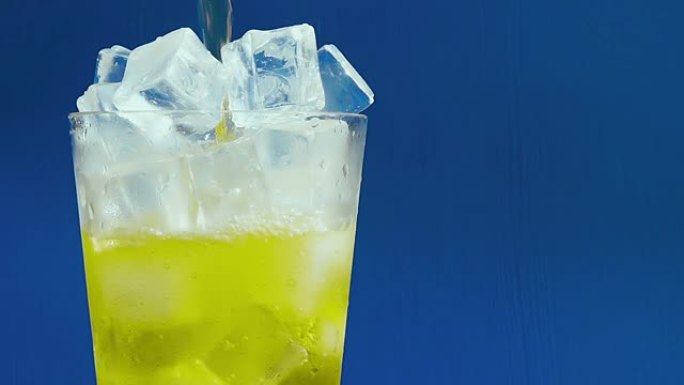 印加可乐苏打水在蓝色背景上慢动作倒入一杯冰中