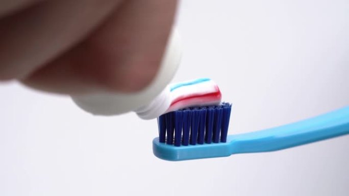 一个男人将彩色牙膏从管子上挤到牙刷上的特写镜头。孤立，在白色背景上
