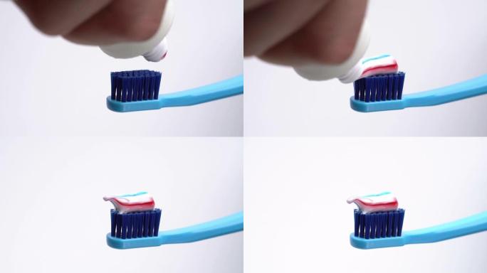 一个男人将彩色牙膏从管子上挤到牙刷上的特写镜头。孤立，在白色背景上