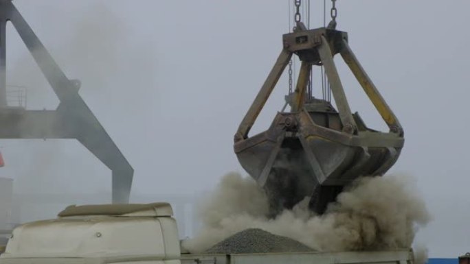 在河港将水泥熟料从船上卸载到卡车的抓斗起重机。驳船运送尘土飞扬的散装货物。龙门起重机在室外港口卸载和